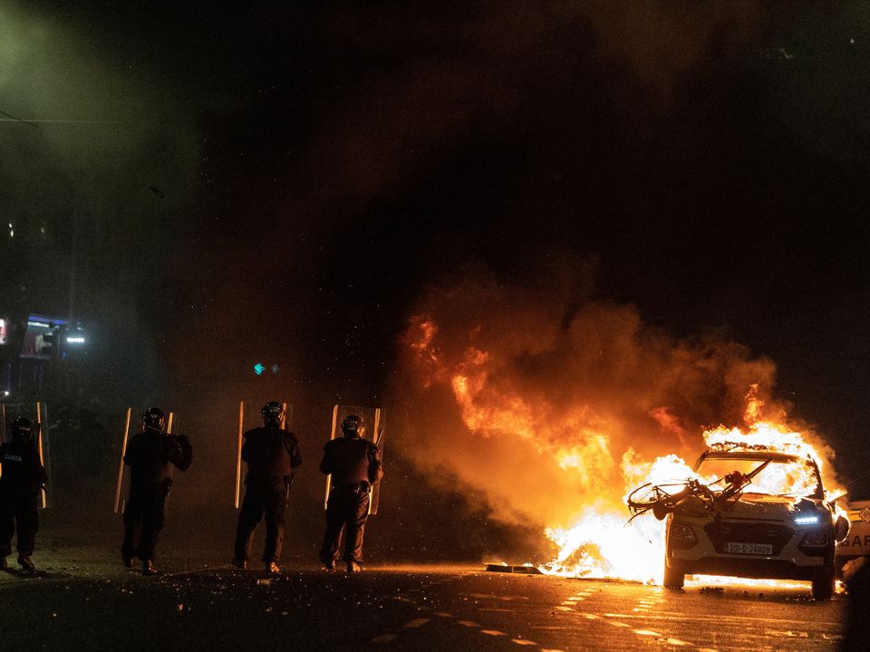 Riot officers face down demonstrators next to a burning garda car near Parnell Square in Dublin. Photo: Clodagh Kilcoyne/Reuters